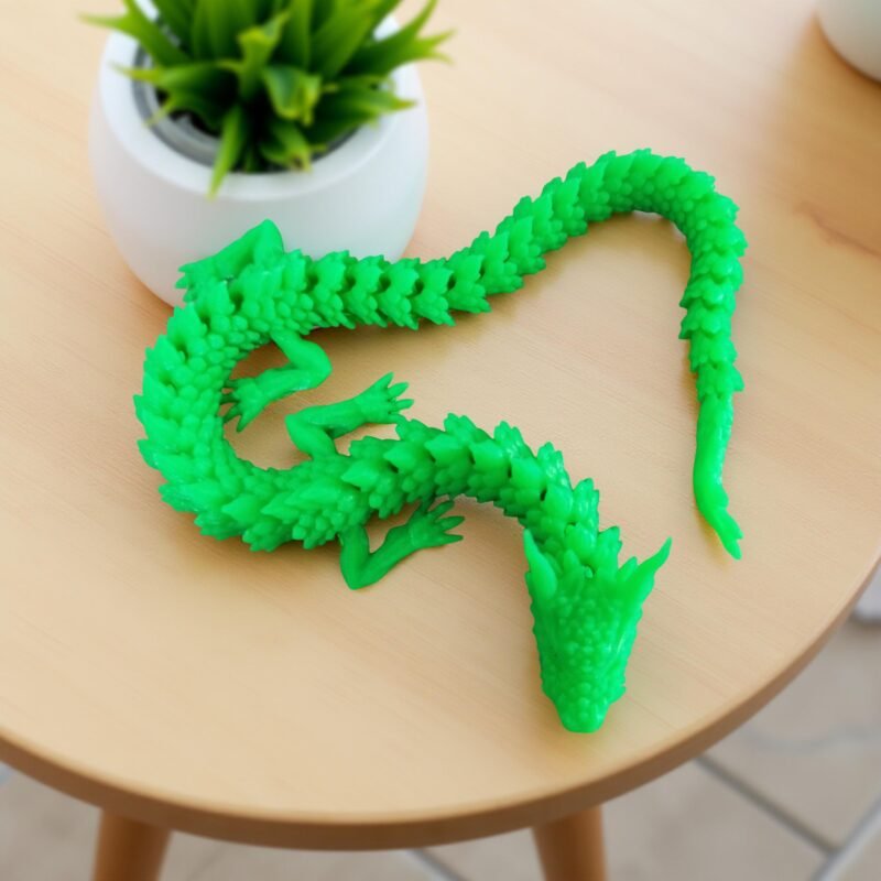 Dragão verde impresso em 3D, segurado na mão, com plantas suculentas ao fundo